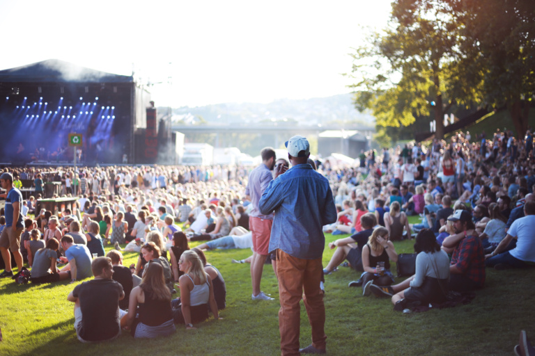 Mann med caps står og kikker ut over et folkehav i sola på marinen, i bakgrunnen er en konsertcene