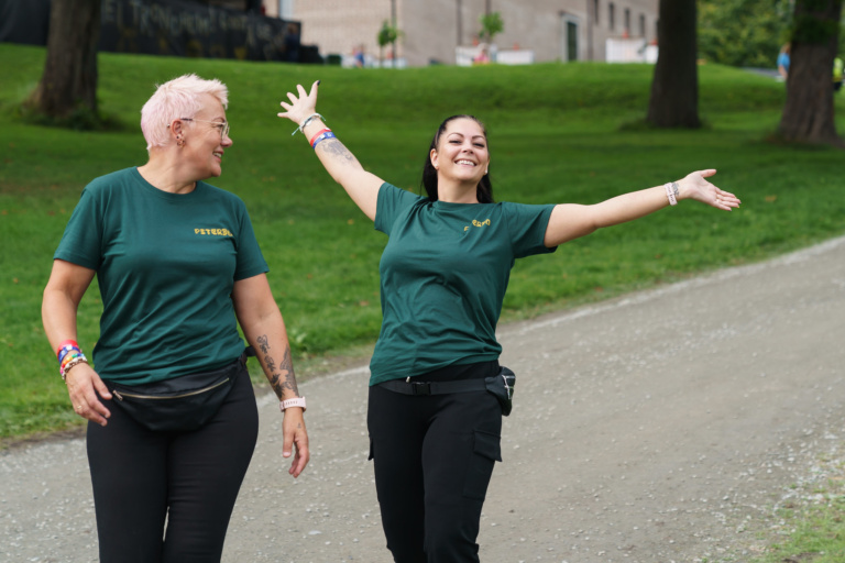 Bildet viser to frivillige på Pstereo, stående i en bakke. Den ene har armene i været og ser glad på kamera.